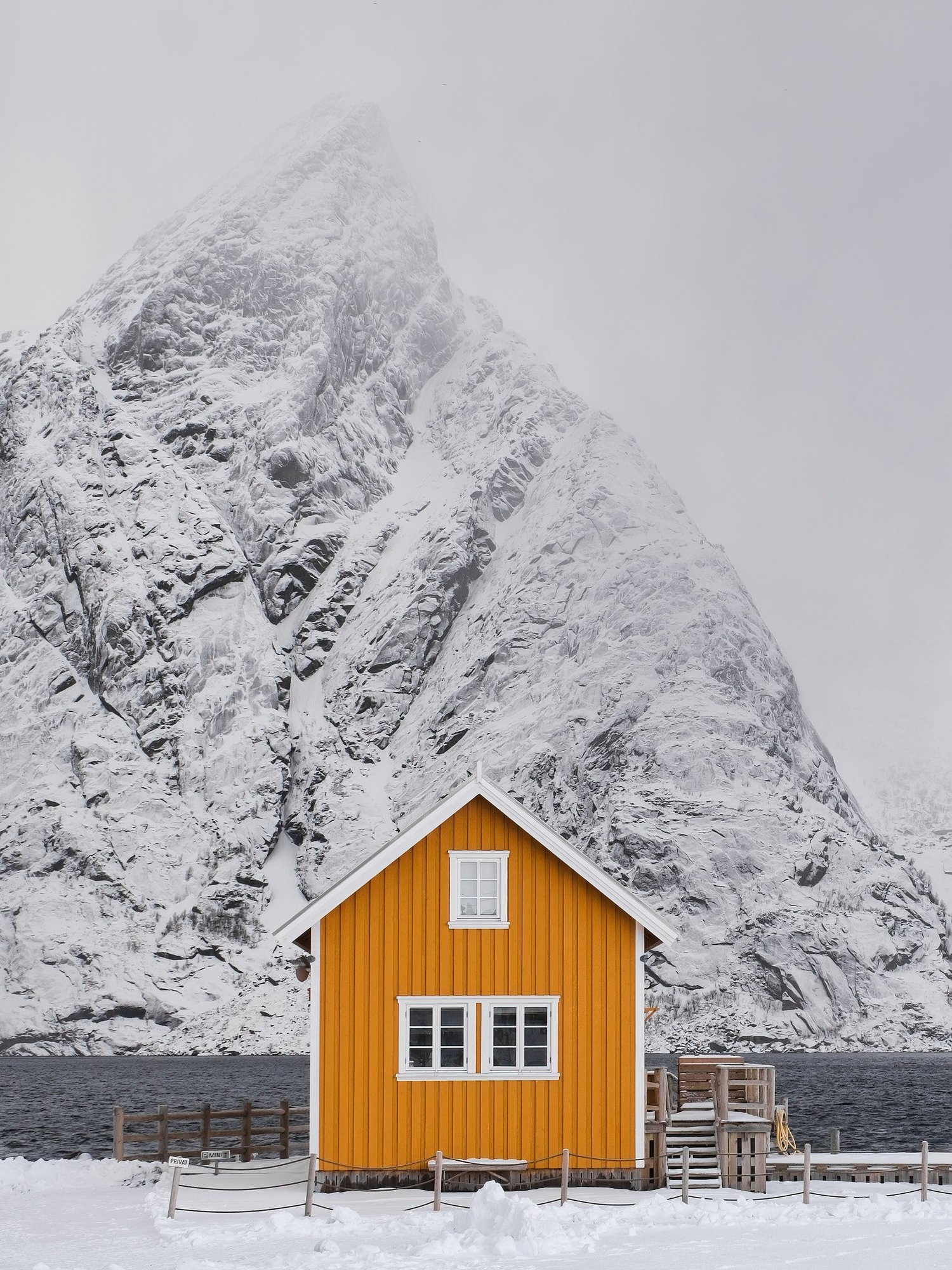Ein gelbes Haus mit weissen Fenstern liegt vor einer verschneiten Bergkulisse.