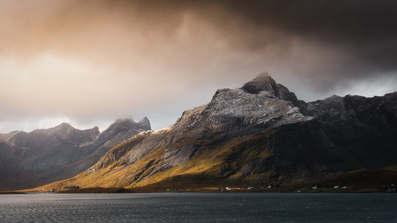 Abendlicht fällt auf die steilen, zerklüfteten Berge der Lofoten; davor liegt dunkles Wasser.