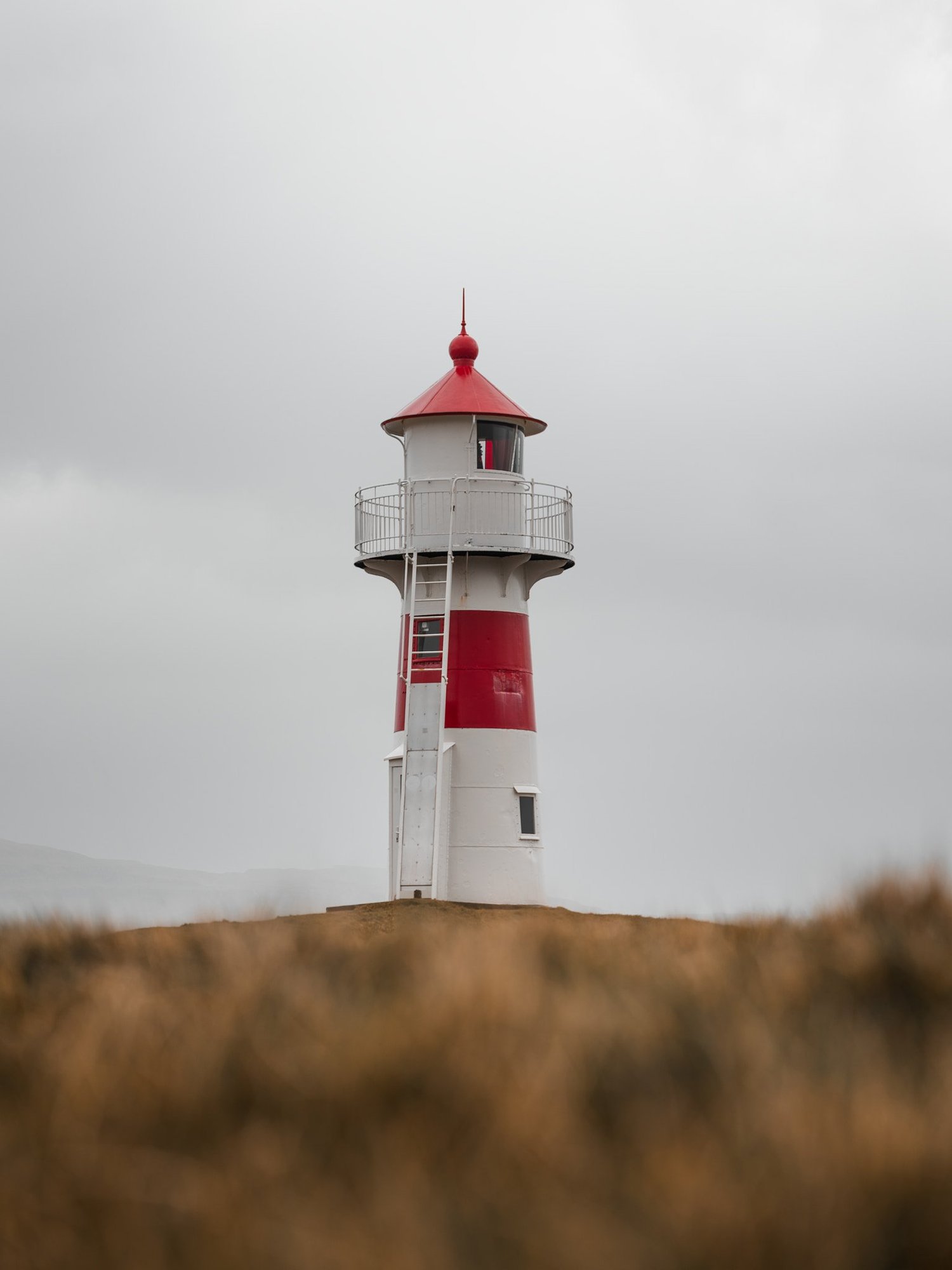 Ein weisser Leuchtturm mit rotem Dach steht auf einer Anhöhe unter einem wechselhaften Himmel.