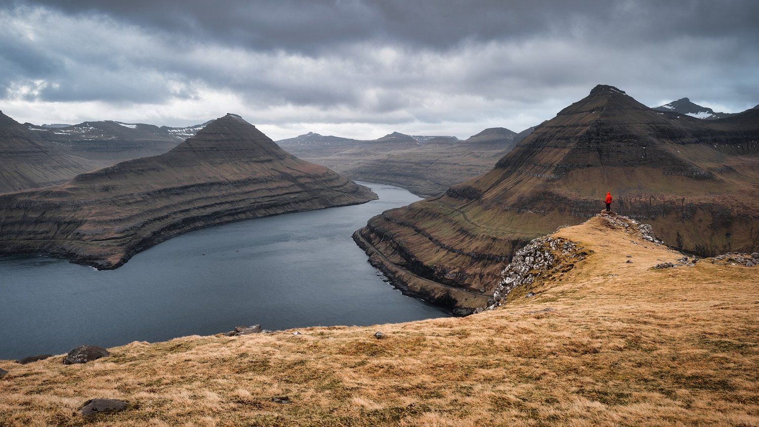Ein Fjord schneidet tief zwischen steilen, mehrfarbigen Klippen und Bergen hindurch.