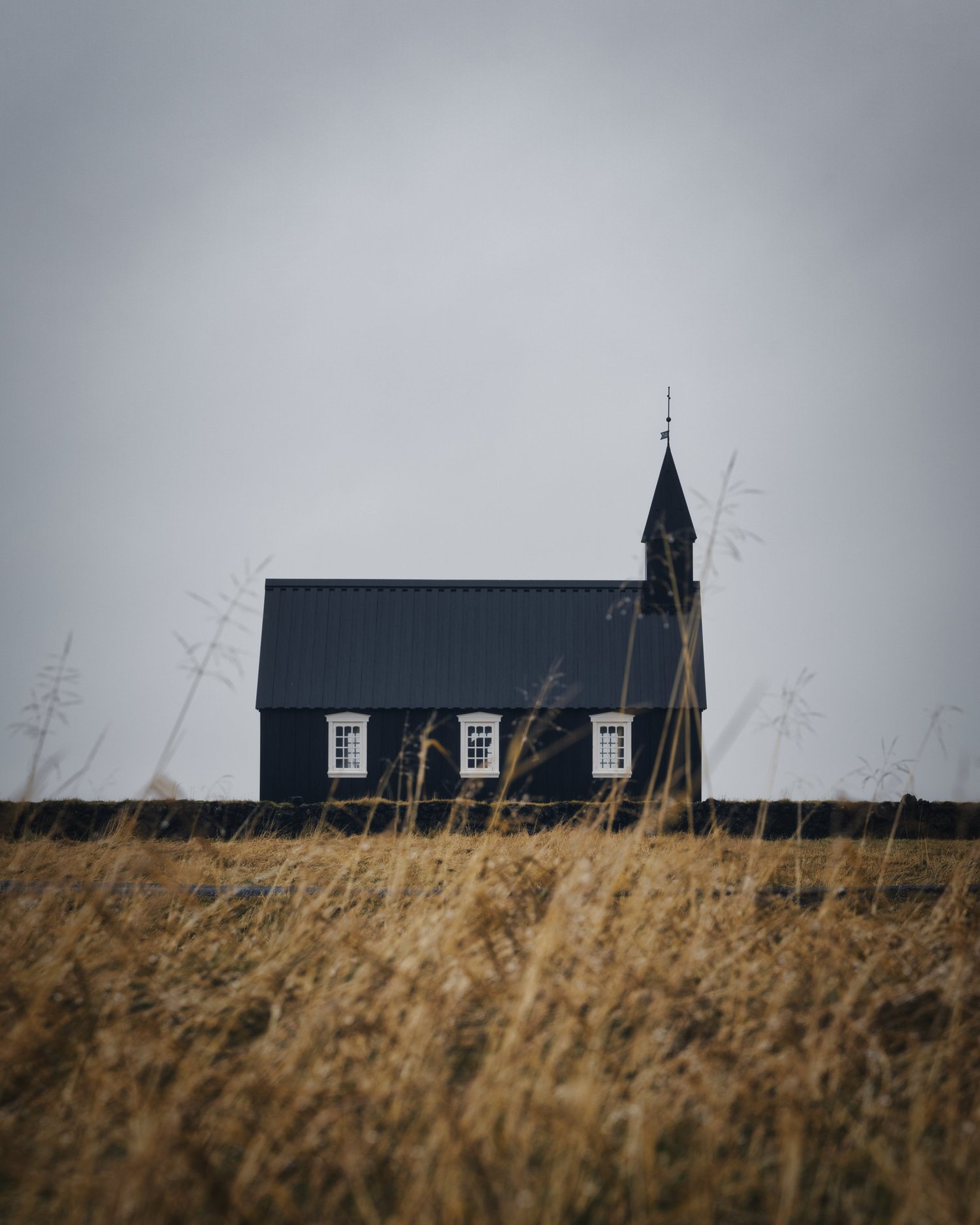 Eine kleine schwarze Kirche mit hellen Fensterrahmen steht im goldenen Gras.