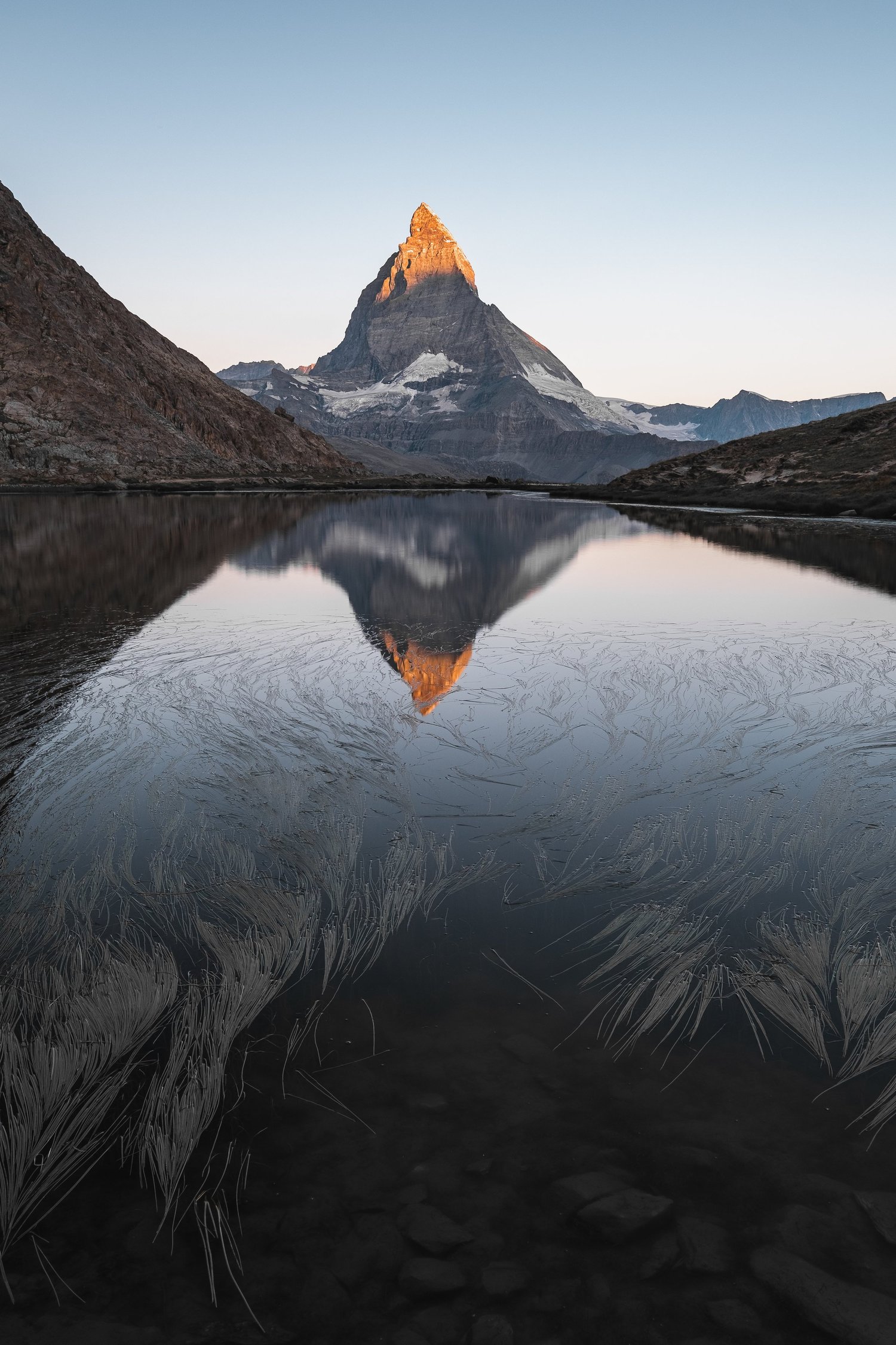 Das Matterhorn leuchtet im ersten Morgenlicht und spiegelt sich im ruhigen Wasser des Riffelsees.